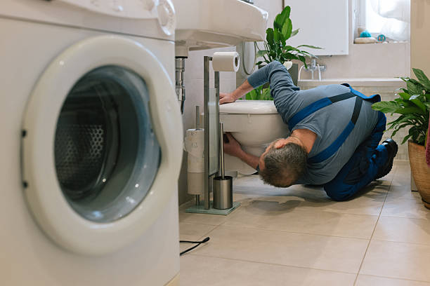 Plumber fixing leak beneath kitchen sink in occupied Cayucos beach home