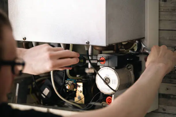 Experienced plumber inspecting water heater controls and connections with precision testing tools