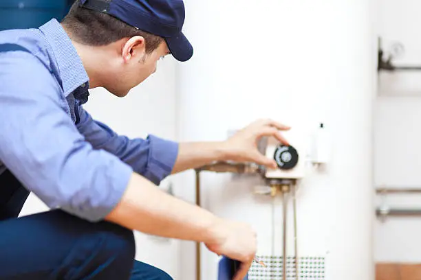 Experienced plumber checking burner assembly and thermostat settings on residential water heater